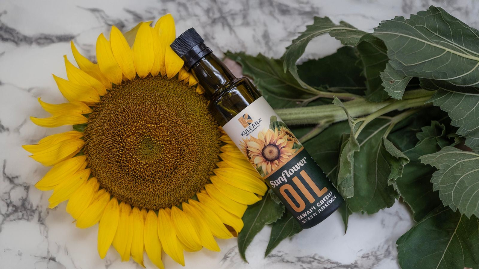 Kuleana Sunflower oil bottle with sunflower and leaves on a marble surface