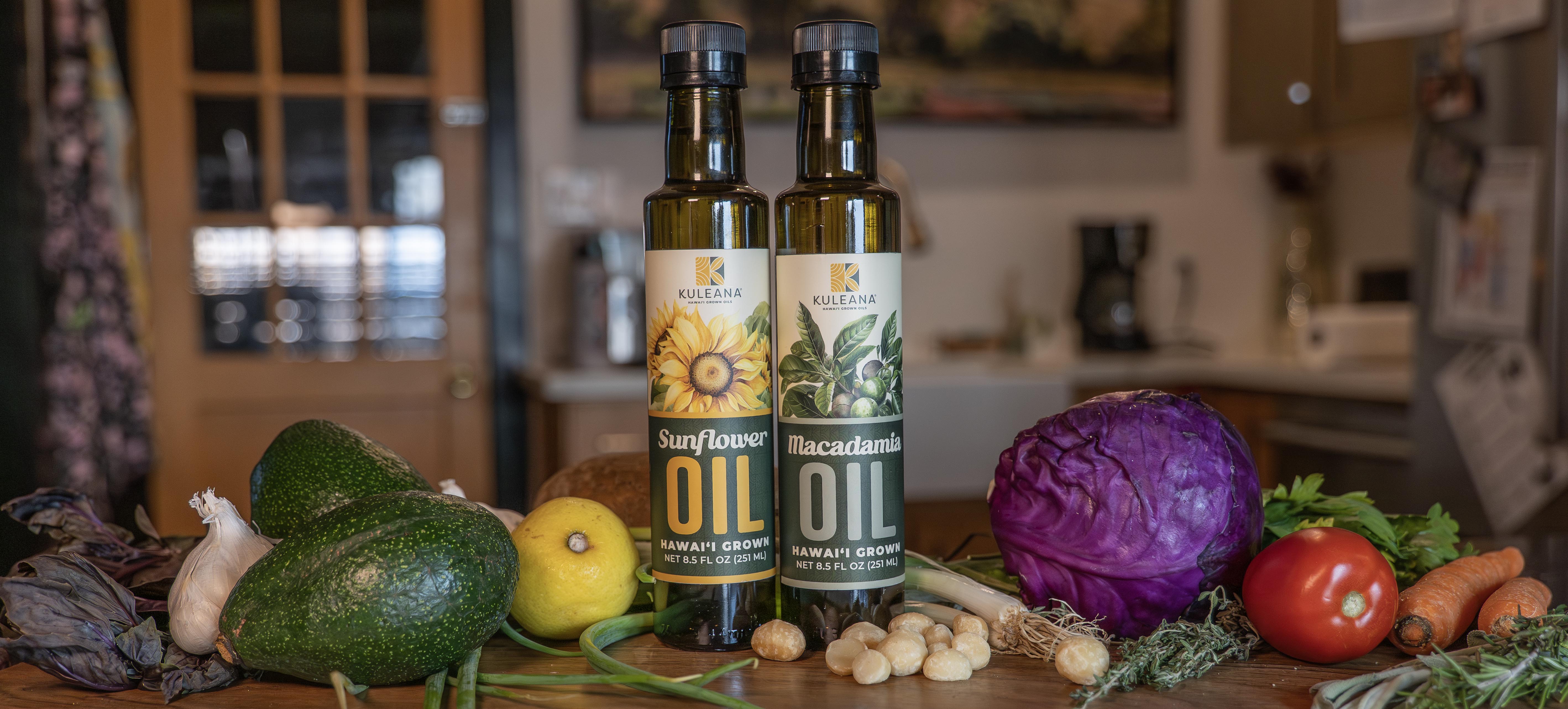 Two bottles of cooking oil on a wooden table with vegetables in a kitchen setting