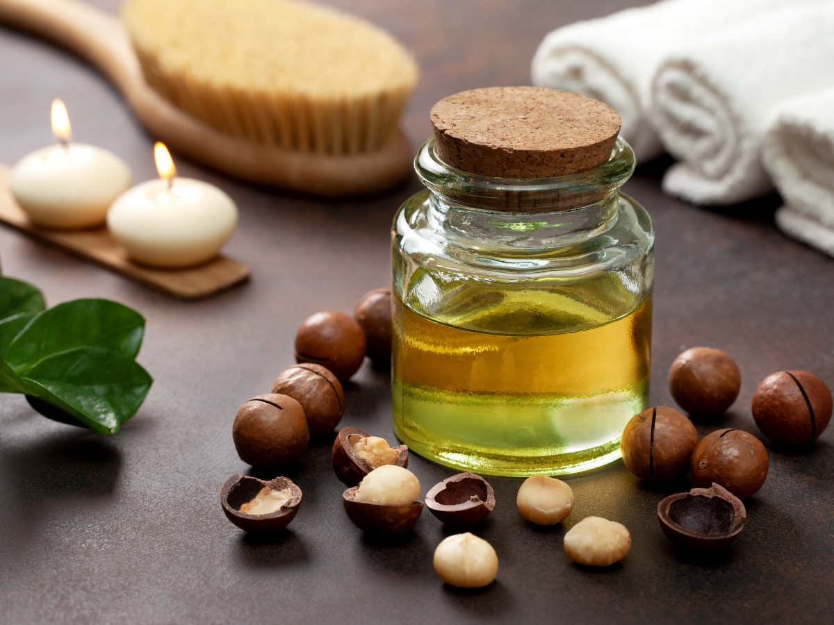 Glass bottle of oil with macadamia nuts and candles on a wooden surface
